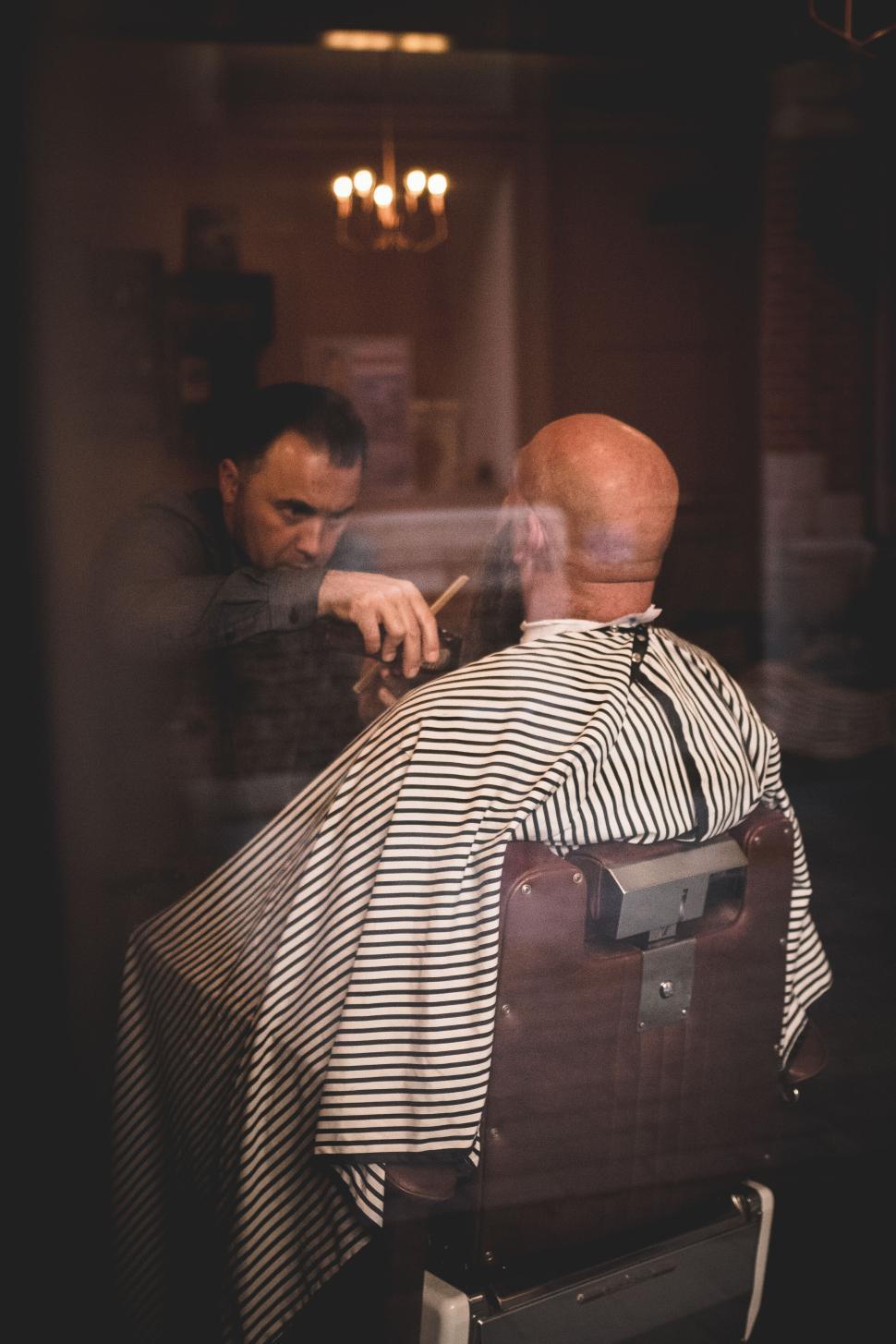 Free Image of Barber cutting man s hair in a classic barbershop setting. 