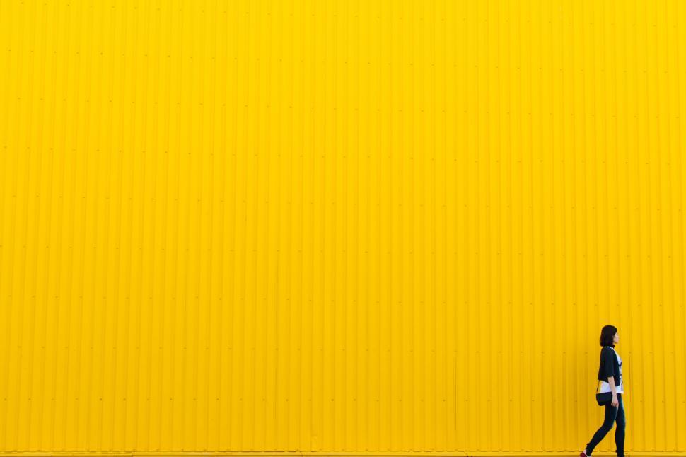 Free Image of Person walking near a bright yellow wall in the daytime 
