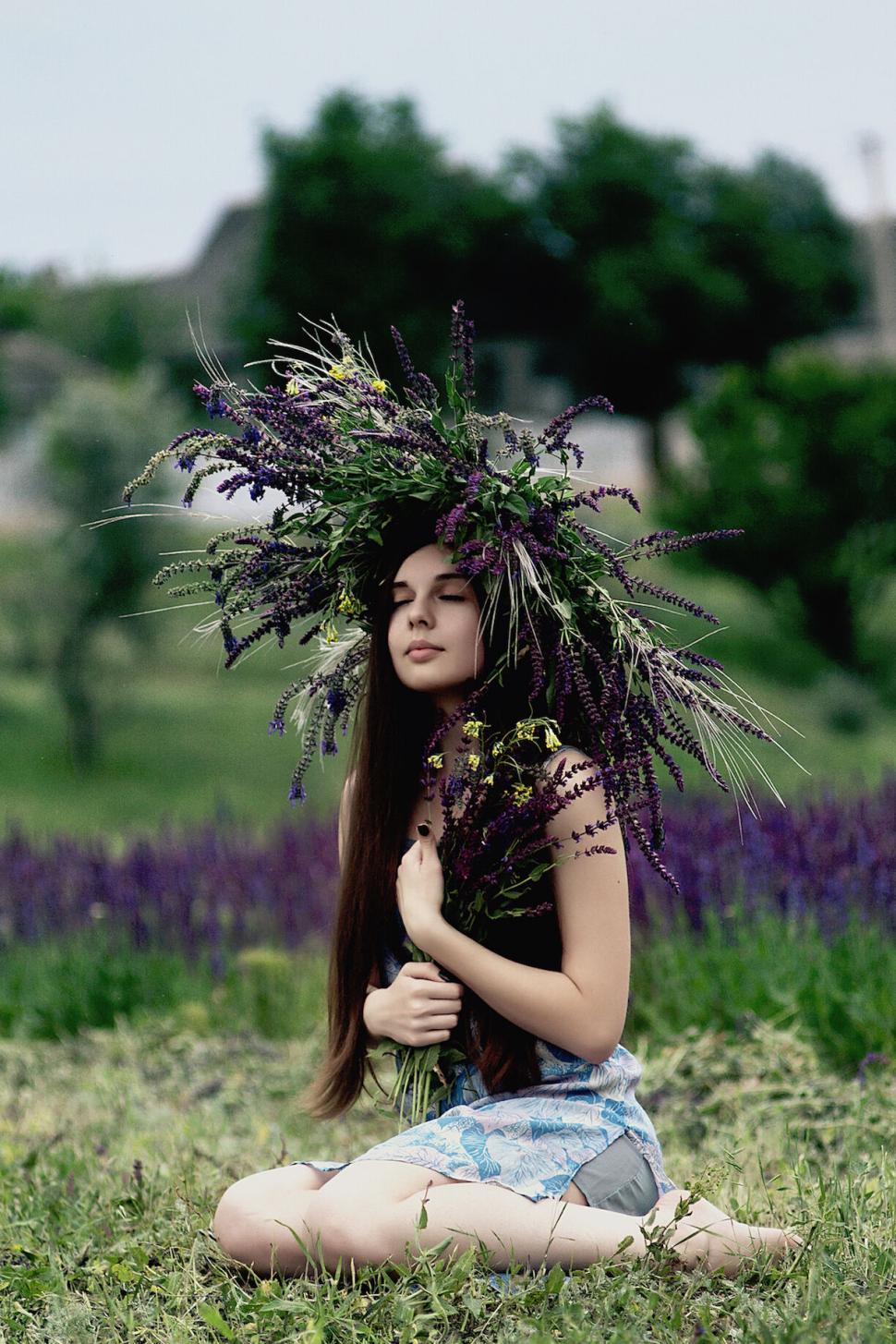 Free Image of Young woman with a floral crown sits in a field peacefully. 