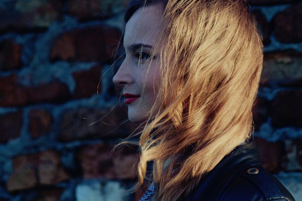 Free Image of Side profile of a woman with red lipstick against brick wall. 