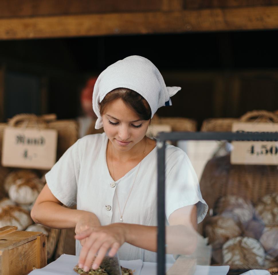 Free Image of Woman in white dress making bread in traditional bakery. 
