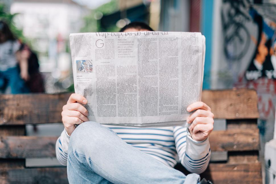 Free Image of Person reading a newspaper on a bench in urban area. 