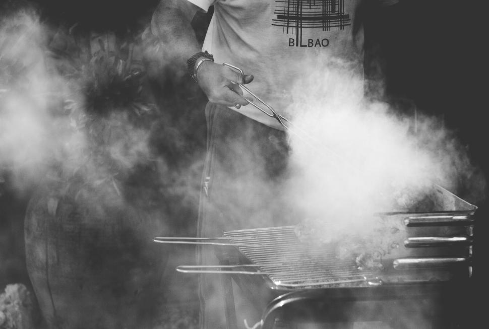 Free Image of Person grilling meat on barbecue with smoke rising 