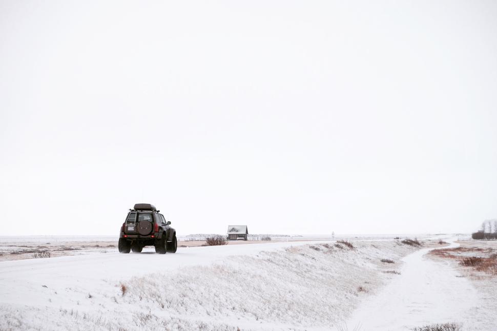 Free Image of Car on snowy road with distant house under cloudy sky. 