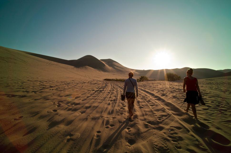 Free Image of Two people walk towards sunlit sand dunes at sunset 