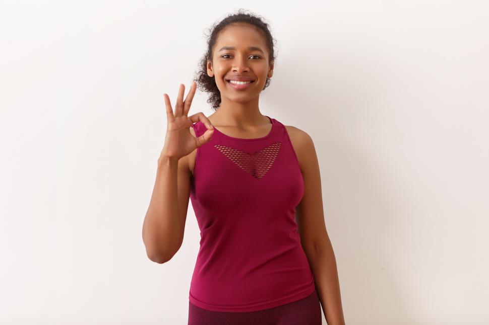 Free Image of Cute young mixed race sportswoman in stylish stretch top expressing approval, confidence, showing okay gesture, feeling full of energy after running workout. Body language and signs concept 