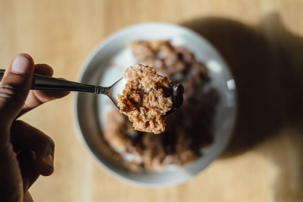 Free Image of Close-up of a spoon with crunchy cereal held over a bowl 