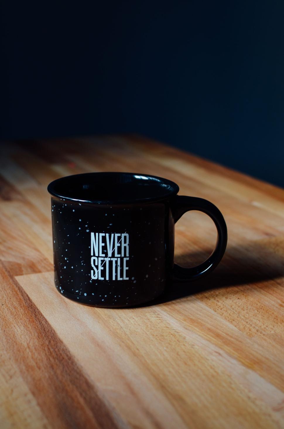 Free Image of Black mug with  Never Settle  text on wooden table. 