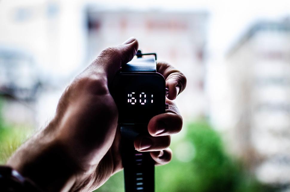 Free Image of Smartwatch displaying time held in hand with backdrop. 