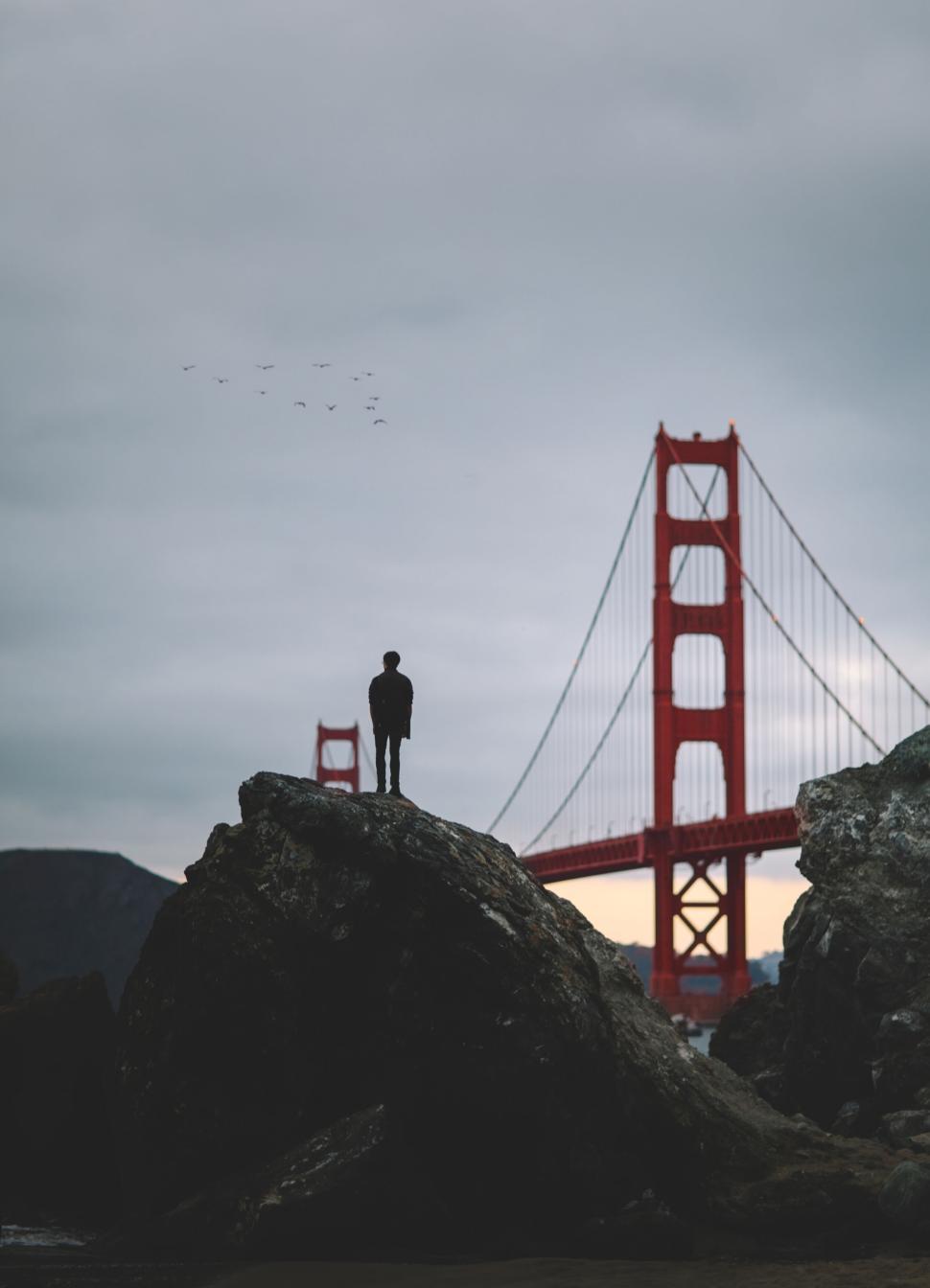 Free Image of Silhouette of a person on rocks near a red bridge. 