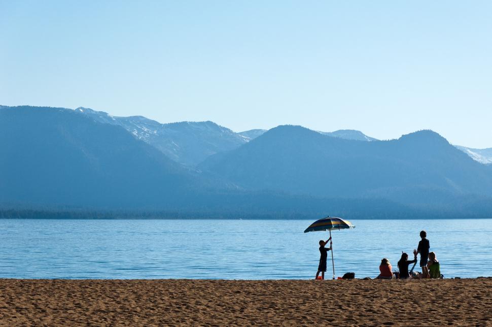 Free Image of Group of people on a sandy beach with mountains behind. 