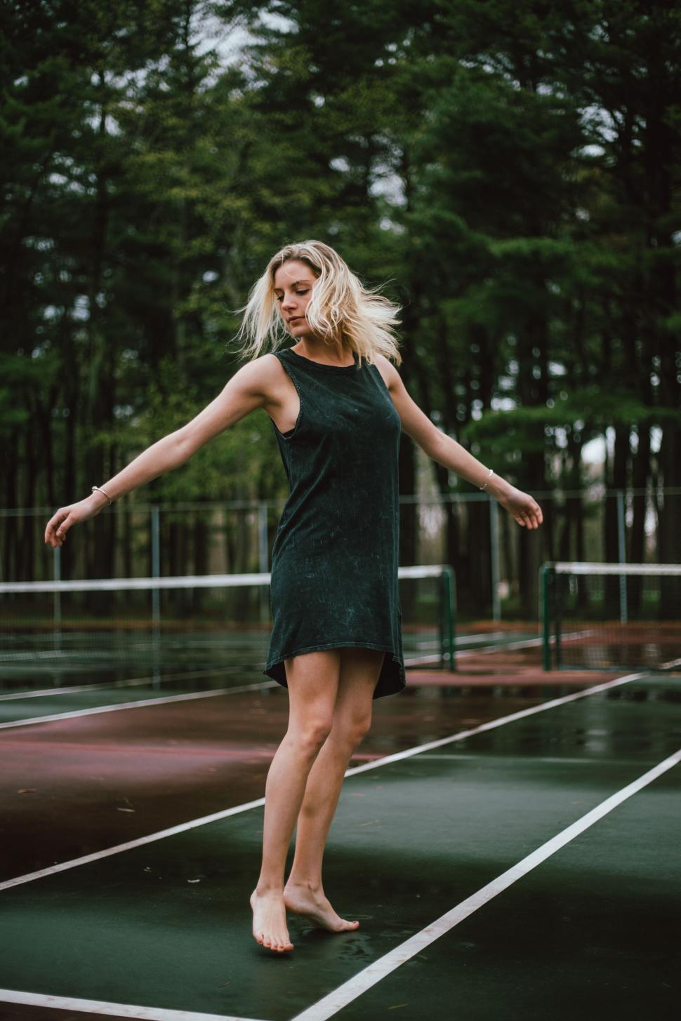Free Image of Woman twirling in a sleeveless dress on wet court 