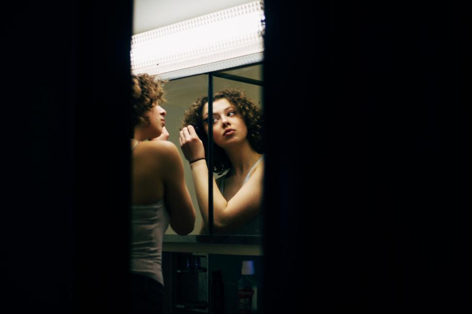 Free Image of Woman applying makeup before a mirror at nighttime 