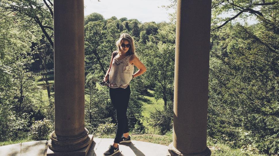 Free Image of Woman posing between columns in outdoor park scenery 