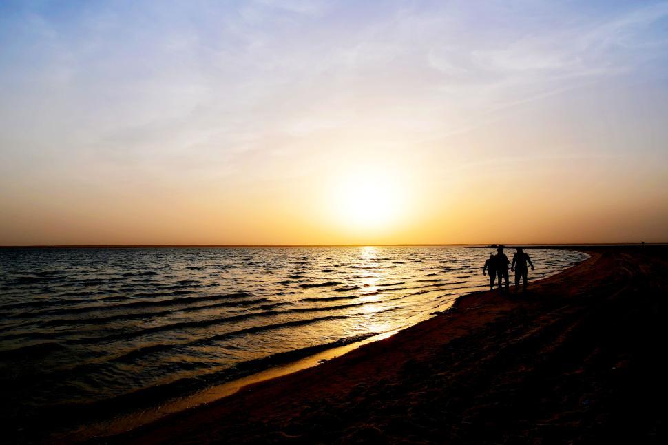 Free Image of Sunset on beach with silhouettes walking by the shore 