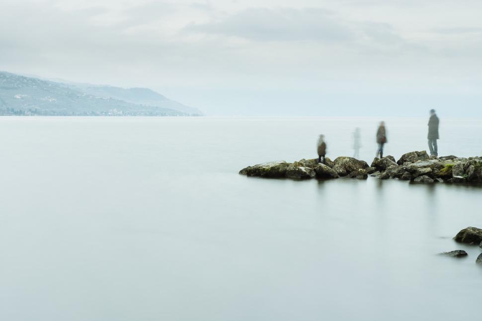 Free Image of People walking, standing on peaceful rocky seashore view 