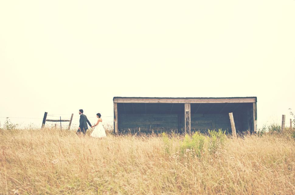 Free Image of Couple walking hand-in-hand in a rural grassy field. 