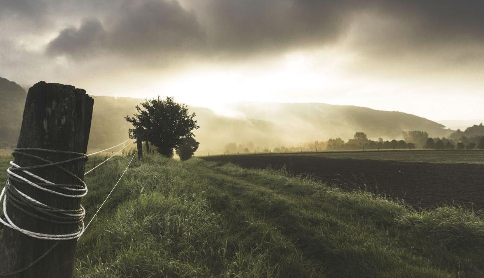 Free Image of Pastoral landscape with fence line under dramatic sky 