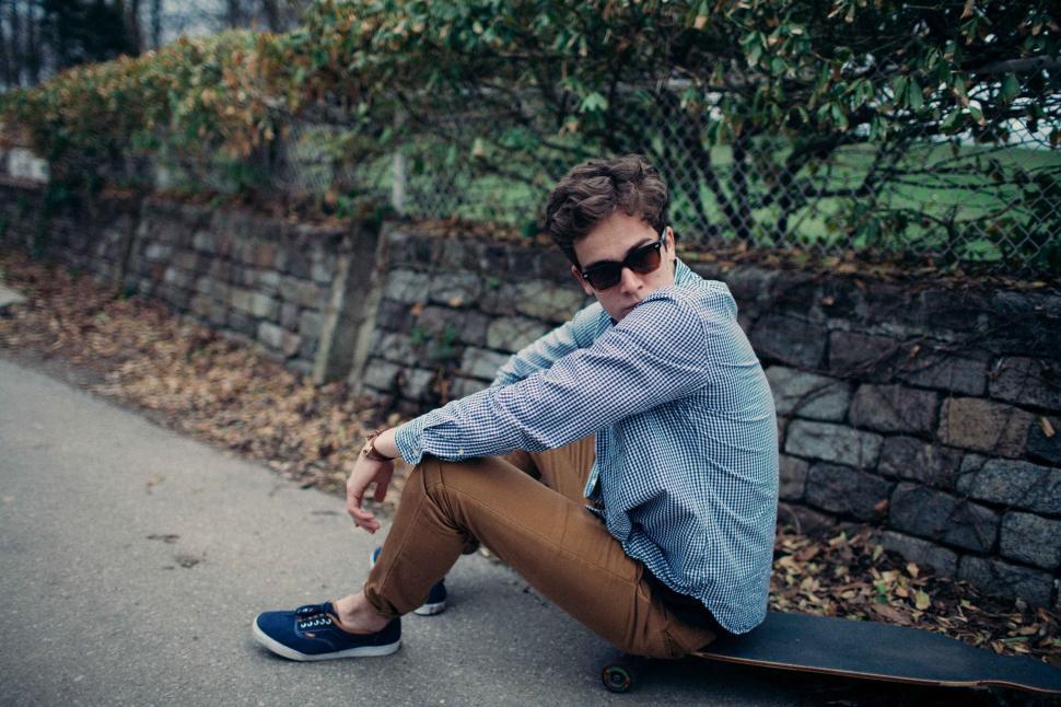Free Image of Man sitting on skateboard by a stone wall outdoors 