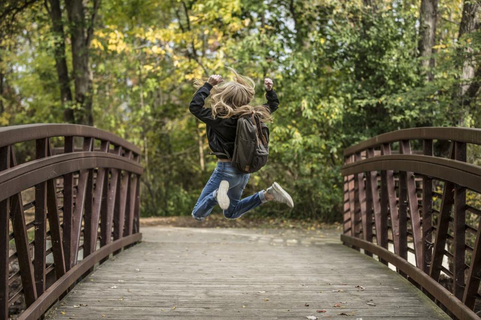 Free Image of Person jumping joyfully on a wooden bridge outdoors. 