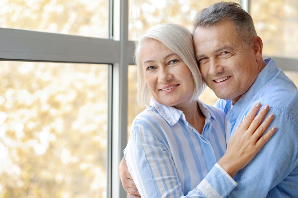 Free Image of Smiling senior couple embracing by a large window 