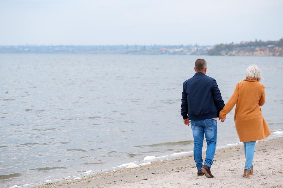 Free Image of Elderly couple walking hand in hand along beach 