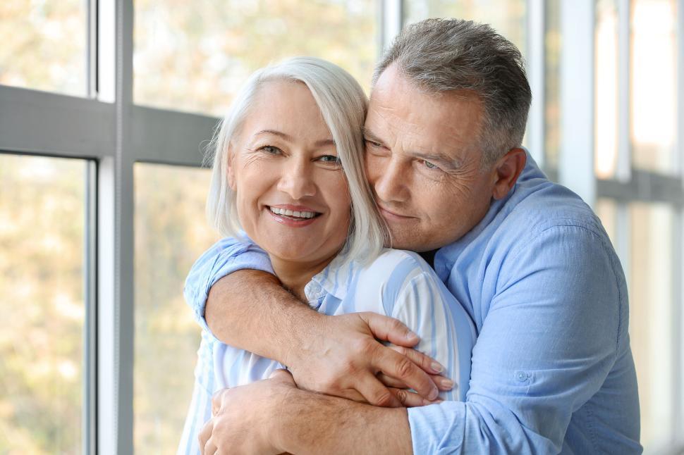 Free Image of Happy couple embracing by a well-lit window, smiling 