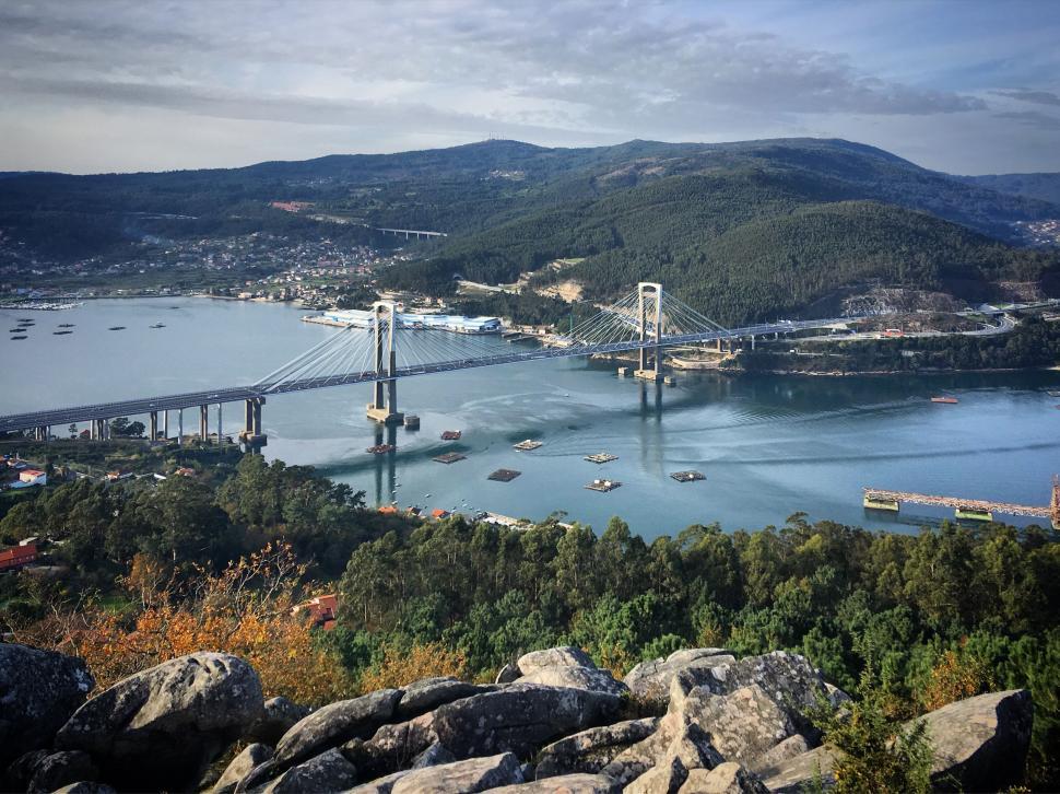 Free Image of Suspension bridge stretching across a wide blue river 