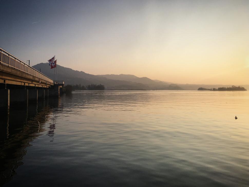 Free Image of Pier extending into calm waters under glowing sunrise sky. 