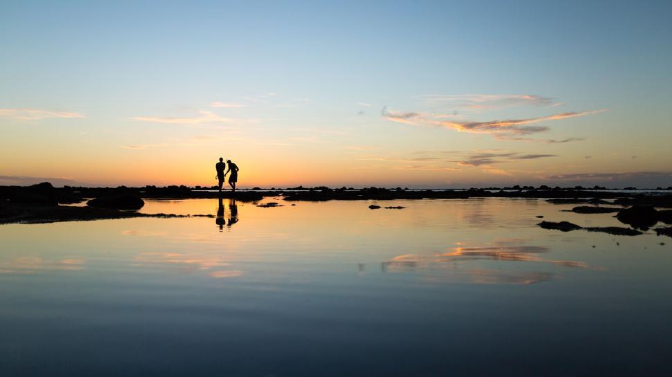 Free Image of Couple standing by the shore at sunset. 