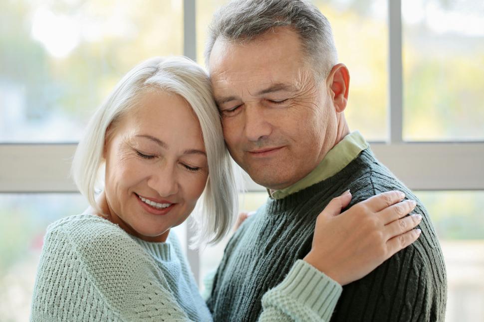 Free Image of Elderly couple sharing a serene hug by the window 