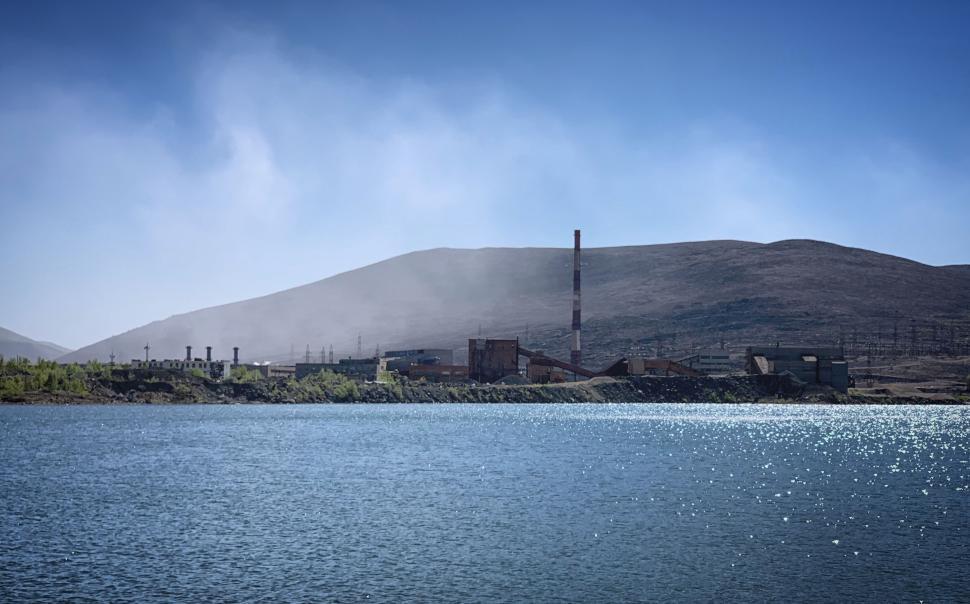 Free Image of Industrial facility by water with hills in background. 