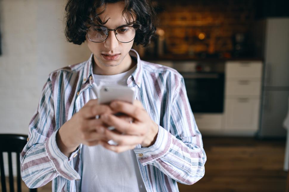 Free Image of Worried serious young man holding smart phone, looking at screen with frustrated facial expression, reading text message, receiving bad news. Stylish guy messaging via online app using mobile 