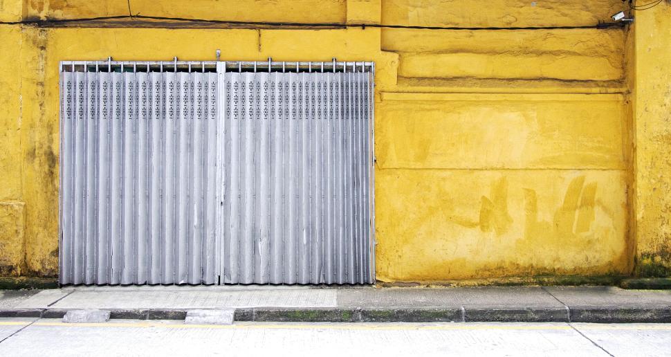 Free Image of Yellow wall with large grey metal folding entry gate 
