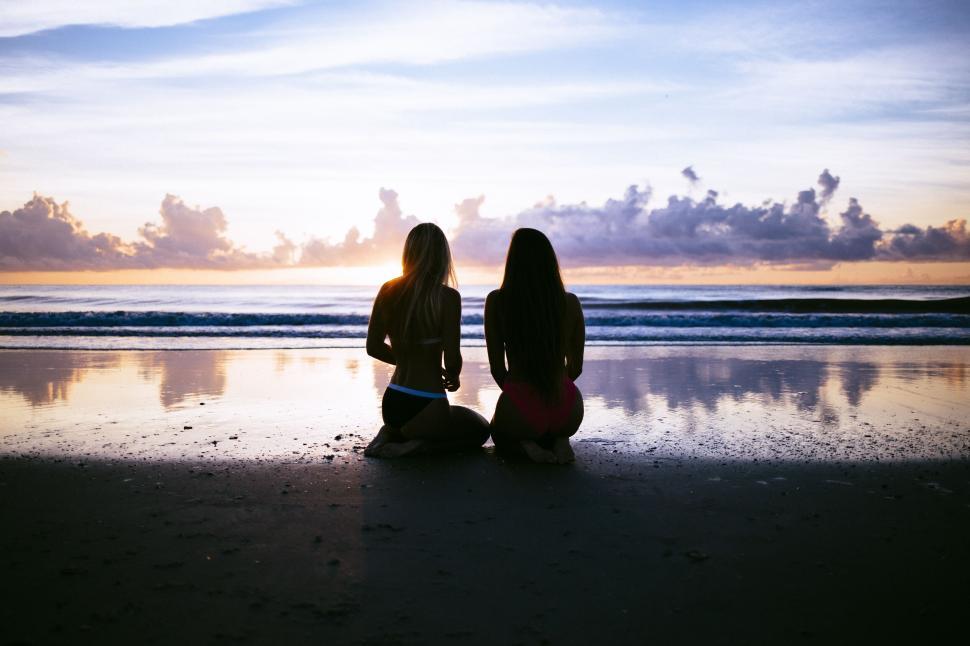 Free Image of Two women sitting on the beach at sunset 