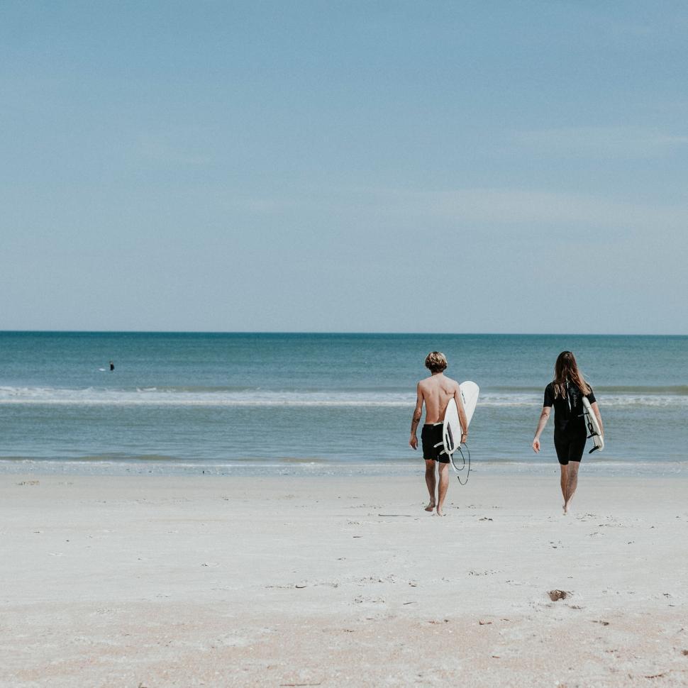 Free Image of Two people walking towards the ocean with surfboards 