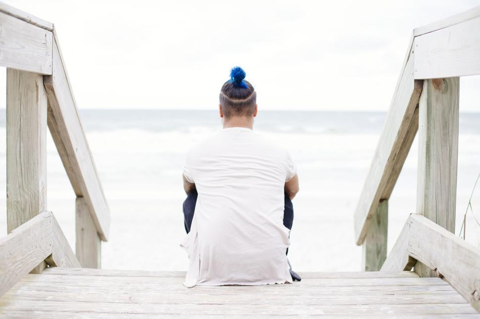 Free Image of Person sitting on boardwalk at beach with blue hair bun 