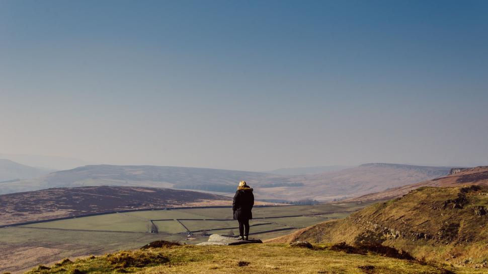 Free Image of Person standing alone on a hilltop with vast landscape 