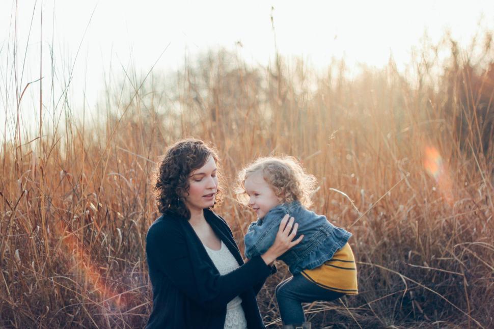 Free Image of Mother lifting her laughing child in a field at sunset. 