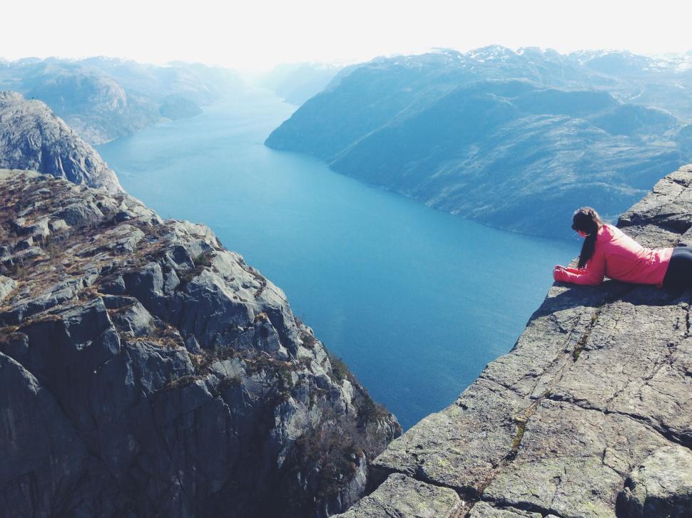 Free Image of Woman laying on cliff edge overlooking a large fjord 