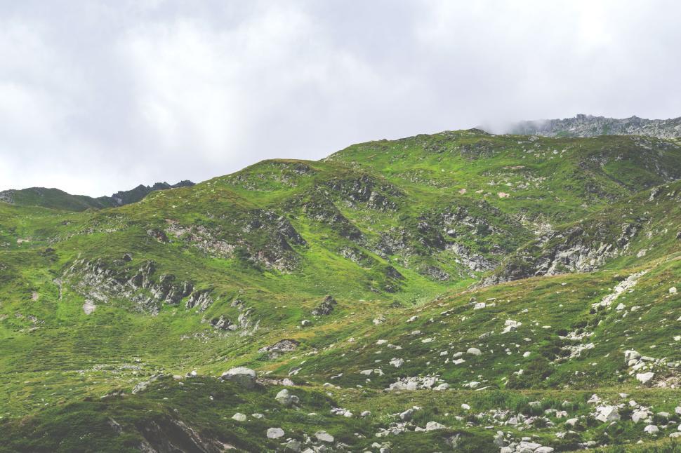 Free Image of Green hills with rocks under cloudy sky, nature calm 