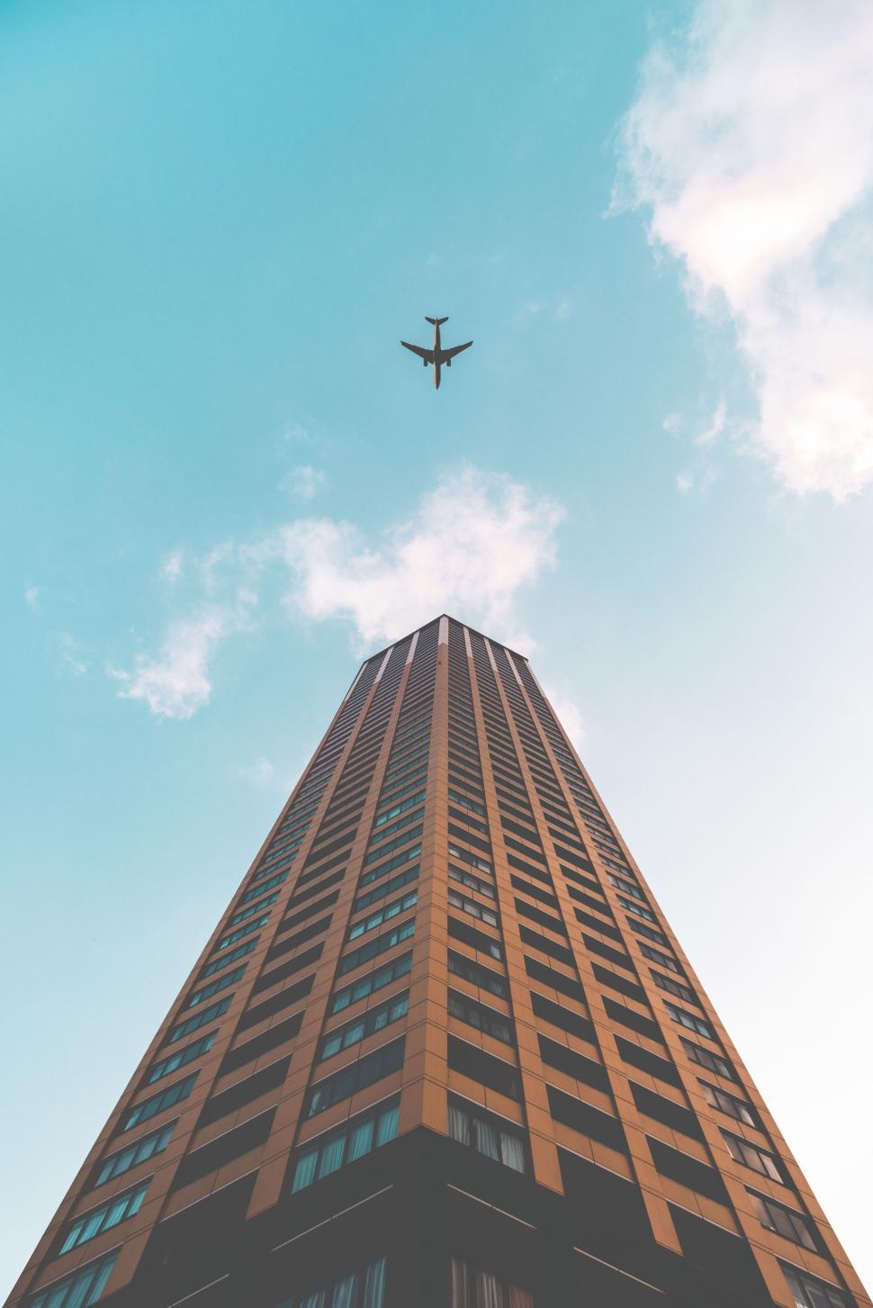 Free Image of Airplane flying above a tall building against clear sky 