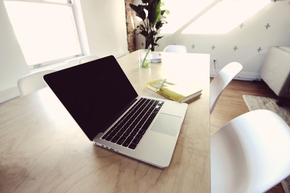 Free Image of Open laptop on wooden desk with a book and plant. 