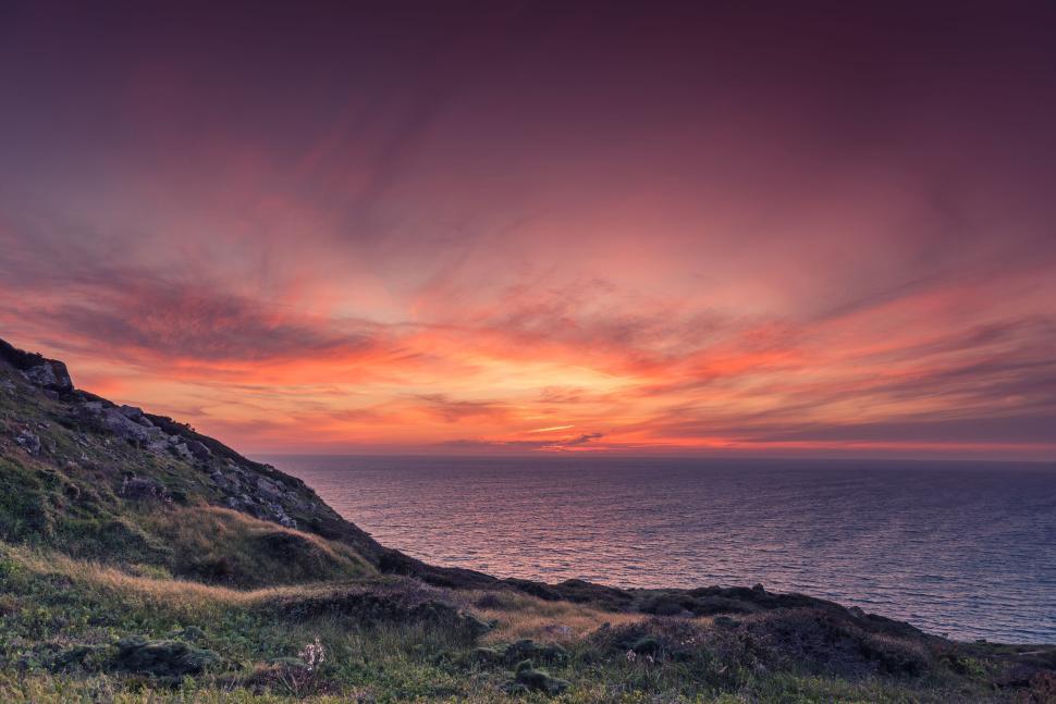 Free Image of Vibrant sunset over ocean and hillside landscape view. 