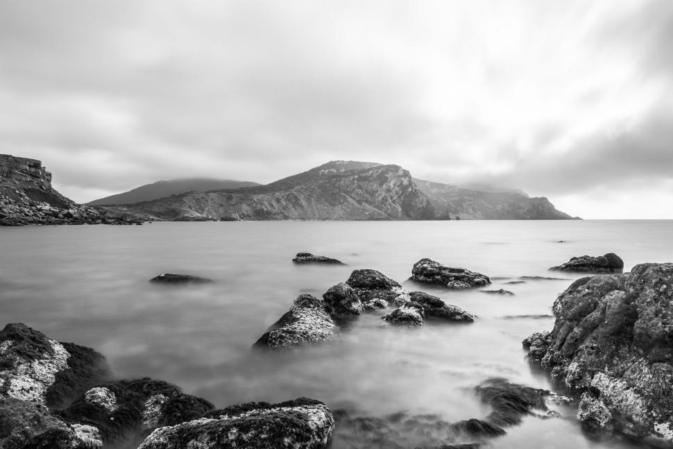 Free Image of Monochrome seascape with rocky shore and distant hills 