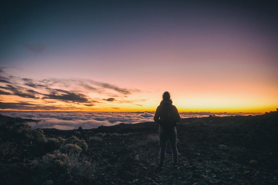 Free Image of Silhouette person at sunrise atop a rocky mountain range 