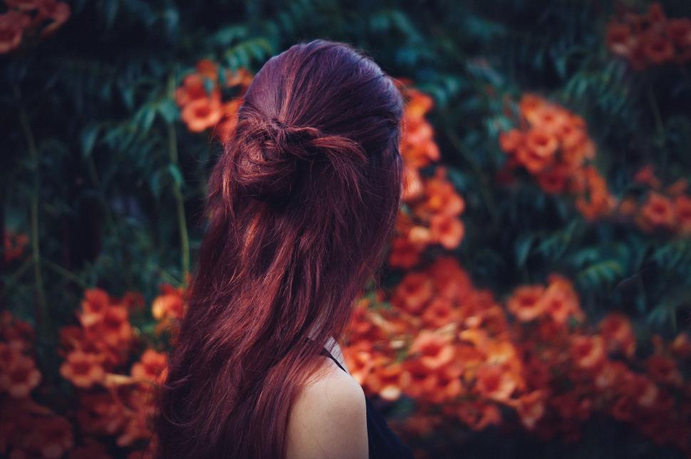Free Image of Woman with red hair stands before floral backdrop, serene. 