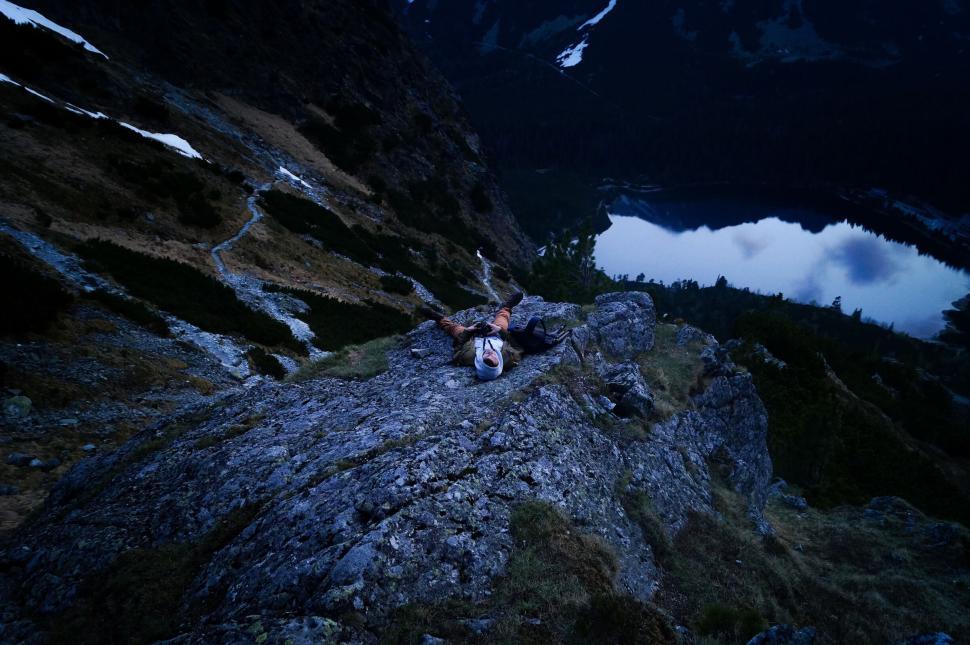 Free Image of Person lying on rock above a scenic mountain lake view 