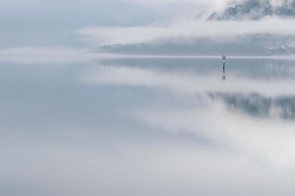 Free Image of Foggy lake with distant mountains and a marker post 