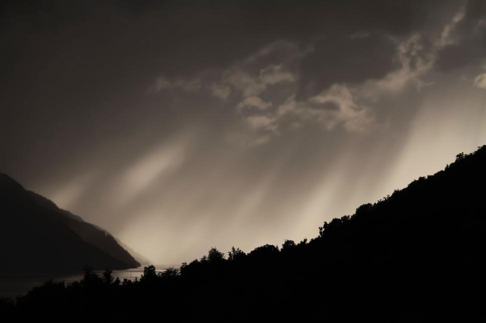 Free Image of Dramatic light rays breaking through clouds over hills 